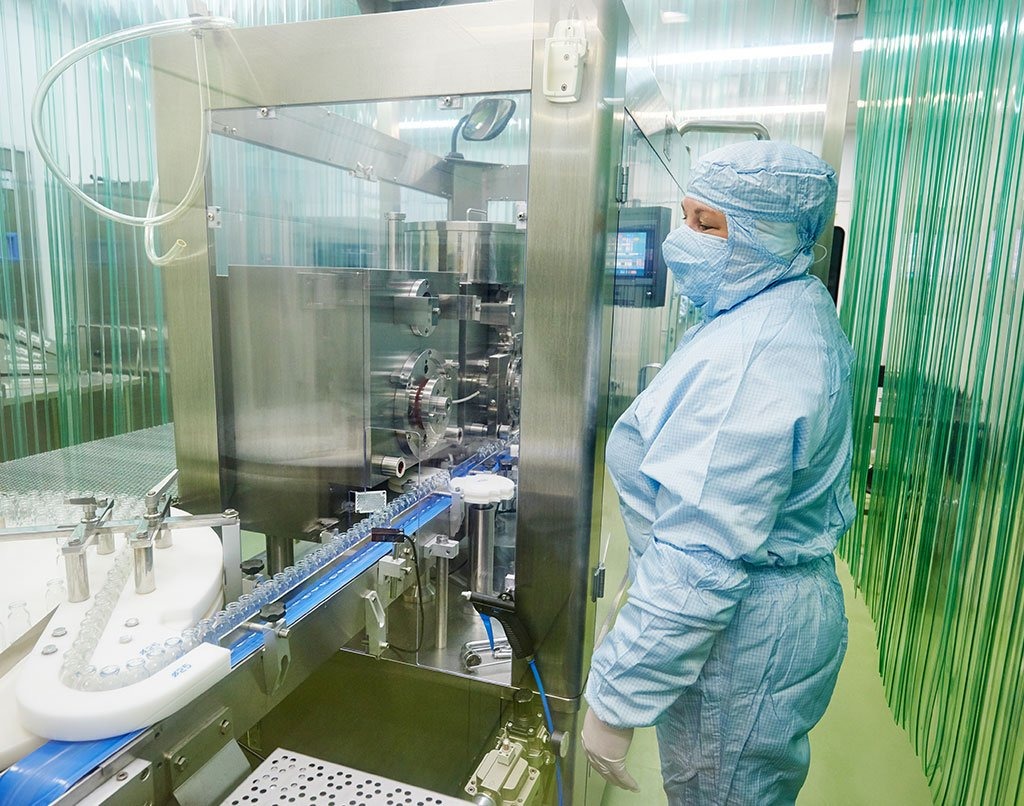 Air sampler certification — masked technician operating pharmaceutical equipment in cleanroom